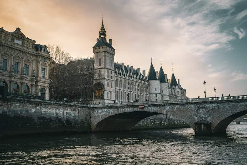 View of the historic Conciergerie and Pont au Change in Paris during a picturesque sunset over the Seine River.