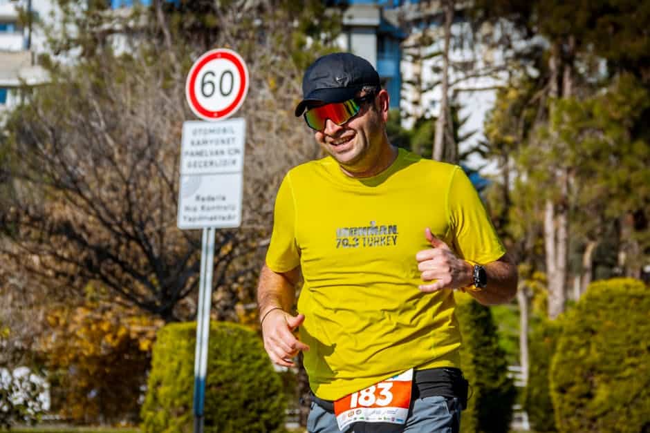 Smiling triathlete running with number bib in a sunny outdoor race, wearing vibrant gear.