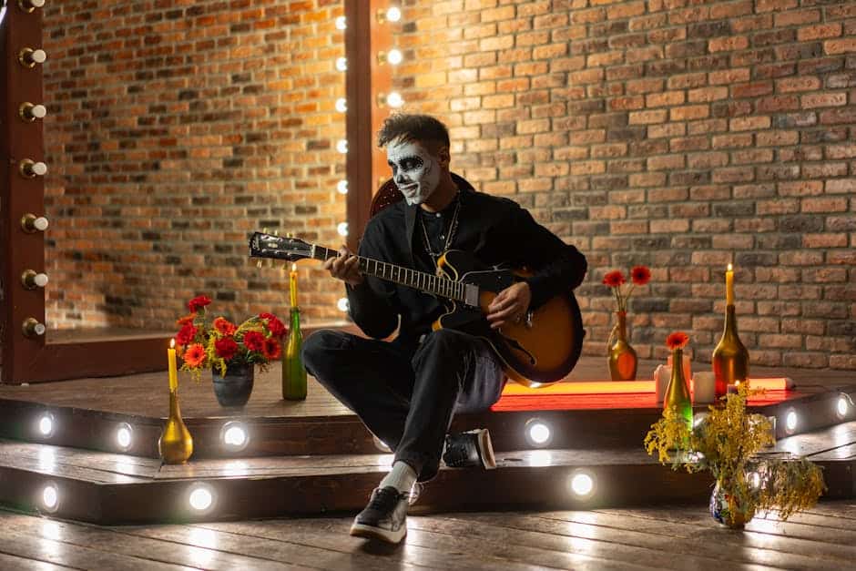 Musician with sugar skull makeup plays guitar on stage, surrounded by candles and flowers.
