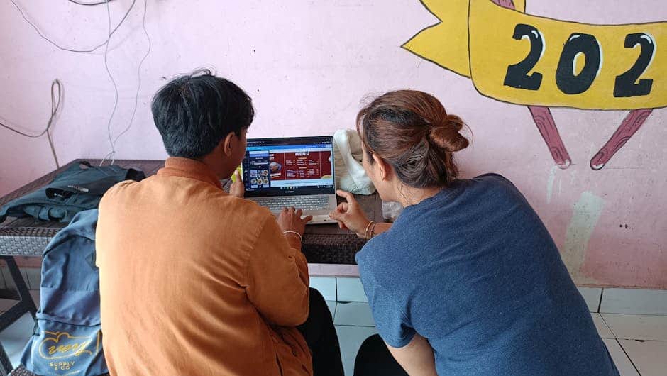 A couple sits at a cafe in Gianyar, Bali, reviewing a food menu on a laptop.