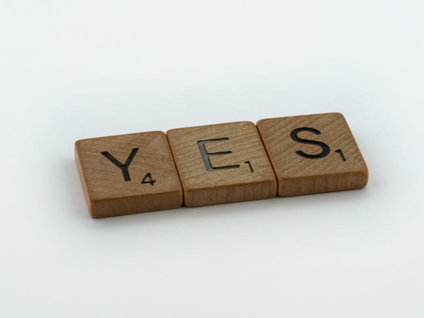 Close-up of wooden Scrabble tiles spelling 'Yes' on a white background.
