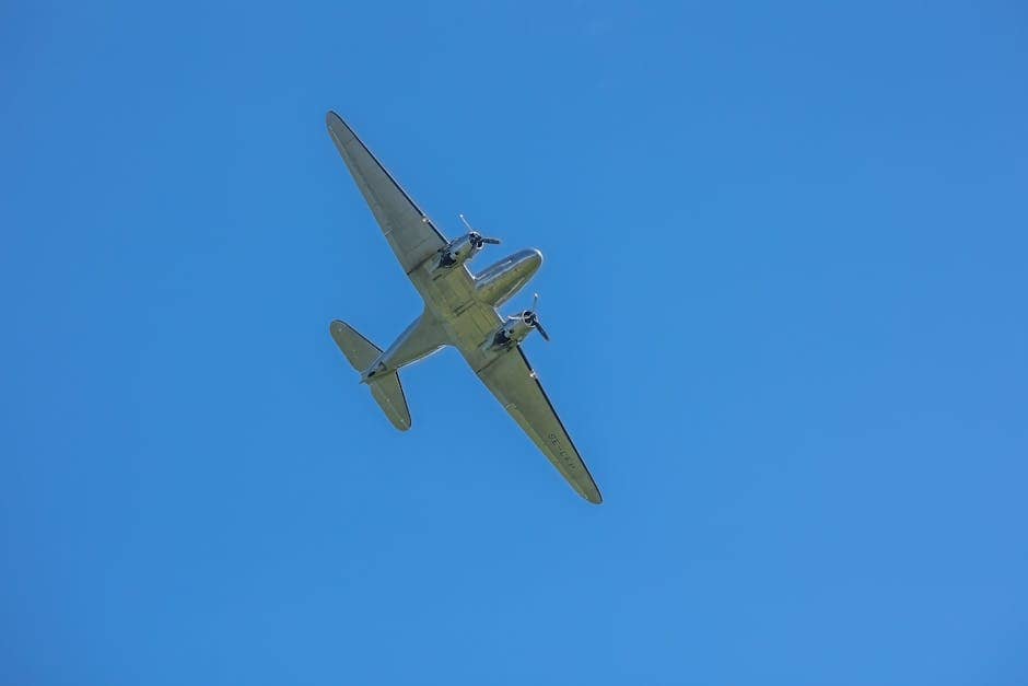 A classic Douglas DC-3 airplane flying above with a clear blue sky backdrop.
