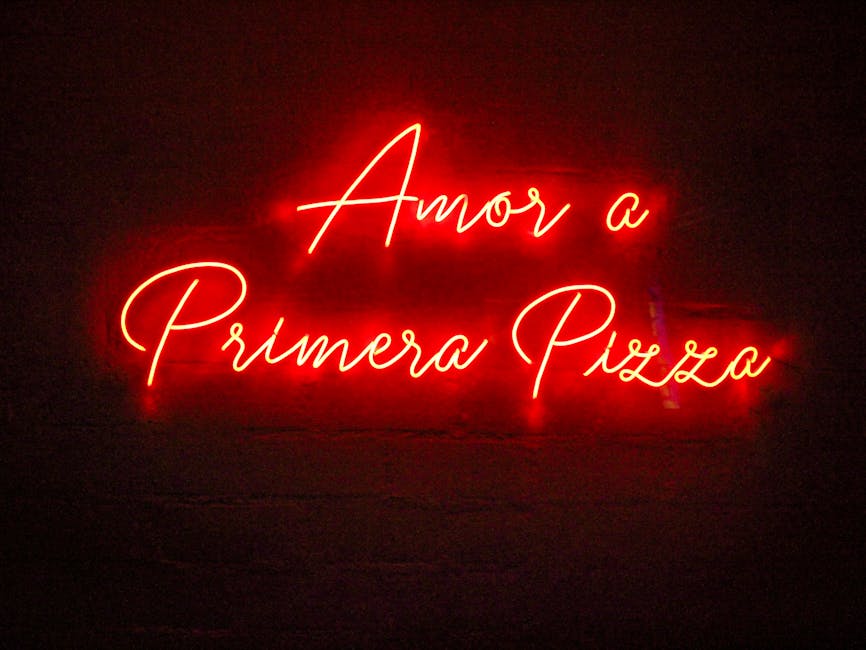 Vibrant red neon sign displaying 'Amor a Primera Pizza' on a dark background, adding a vintage, romantic touch.